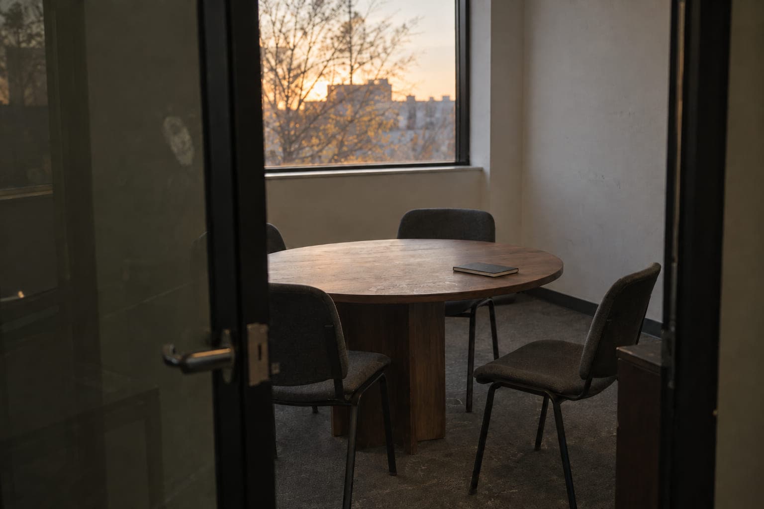 Una sala de reuniones pequeña, vista desde la puerta entreabierta, con la mesa junto a la ventana
